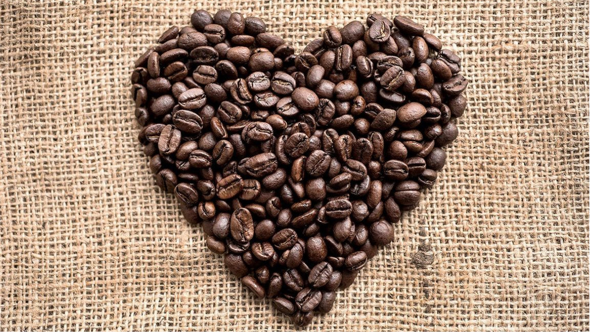 Heart-shaped arrangement of coffee beans on a textured fabric background