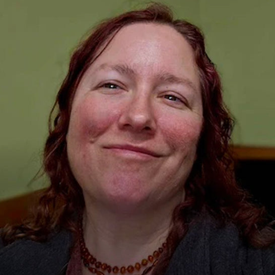 Woman with red hair and freckles smiling against a green wall.