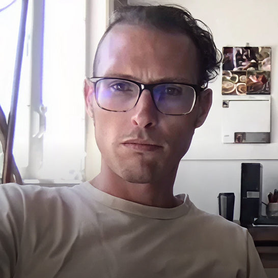 Man wearing glasses in a room with a window and wall decorations.