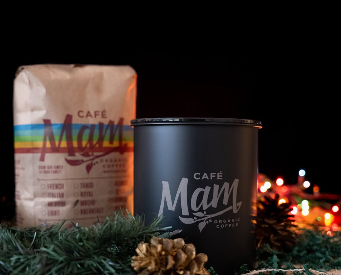 Café Man coffee bag and black tumbler on a dark background with festive lights.