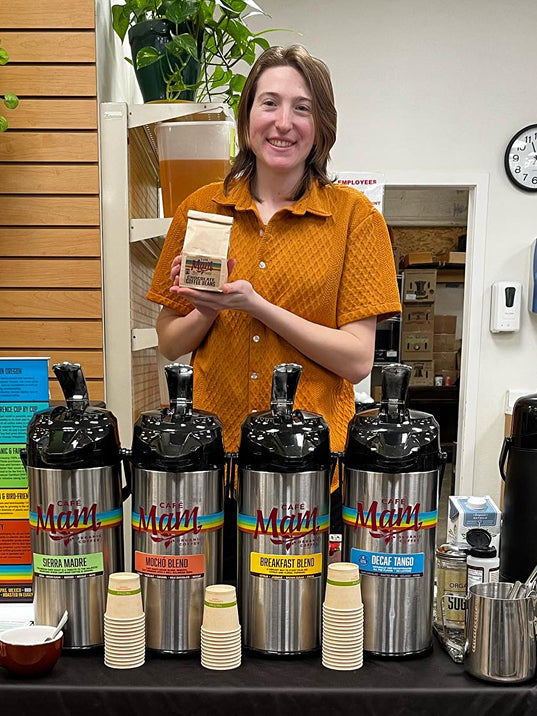Person holding a coffee package in front of coffee dispensers in a store setting