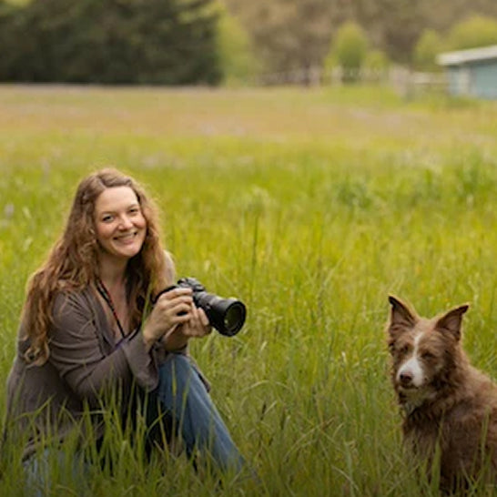Woman holding a camera in a grassy field with a dog