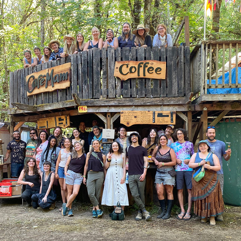 Group of people posing in front of a wooden coffee shop named 'Ole Man Coffee' in a forest setting.