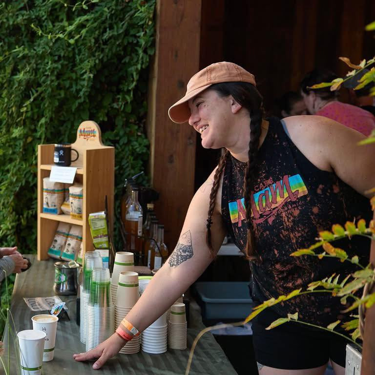Person sitting at a table with cups and bottles, wearing a colorful tank top and hat.
